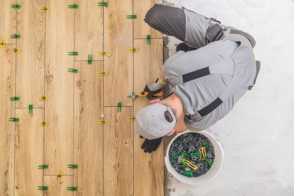 Ceramic Tiles Floor Installer. Wood Like Looking Tiles Installed by Professional Caucasian Construction Interior Finishing Worker. Flooring Industrial Theme.