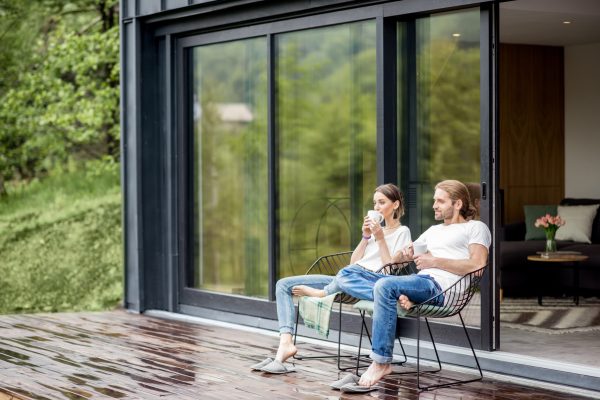 Young couple sitting with cups on the terrace of the modern house enjoying beautiful view outdoors