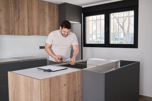 Young argentinian man using measuring tape before placing countertops on modern kitchen.